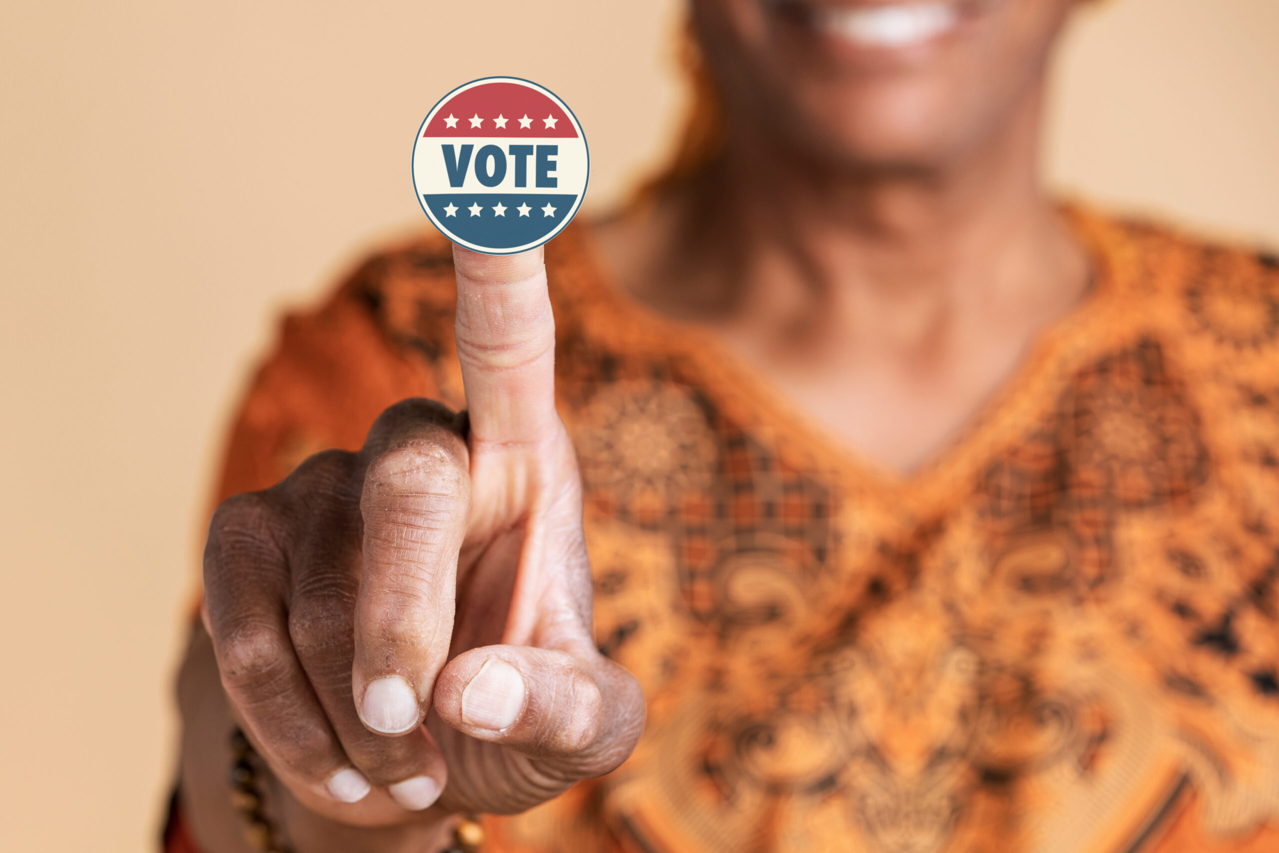 black woman smiling holding up a Vote sticker